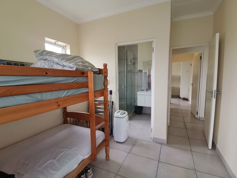 A bedroom featuring tiled flooring and an attached en-suite bathroom with a shower and vanity basin.