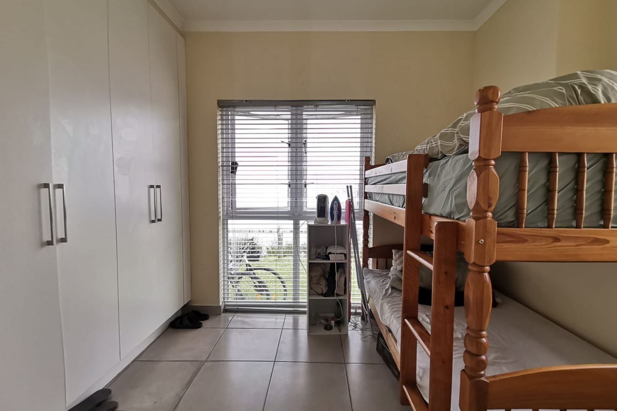 A functional bedroom featuring tiled flooring, built-in cupboards for storage, and a window fitted with venetian blinds.