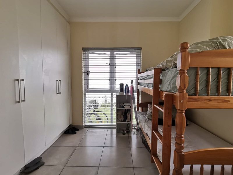 A functional bedroom featuring tiled flooring, built-in cupboards for storage, and a window fitted with venetian blinds.