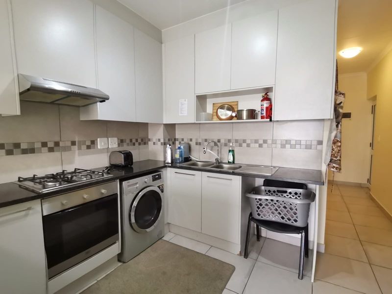 Compact kitchen featuring modern white cabinetry, granite countertops, a gas hob, electric oven, and integrated space for a washing machine.