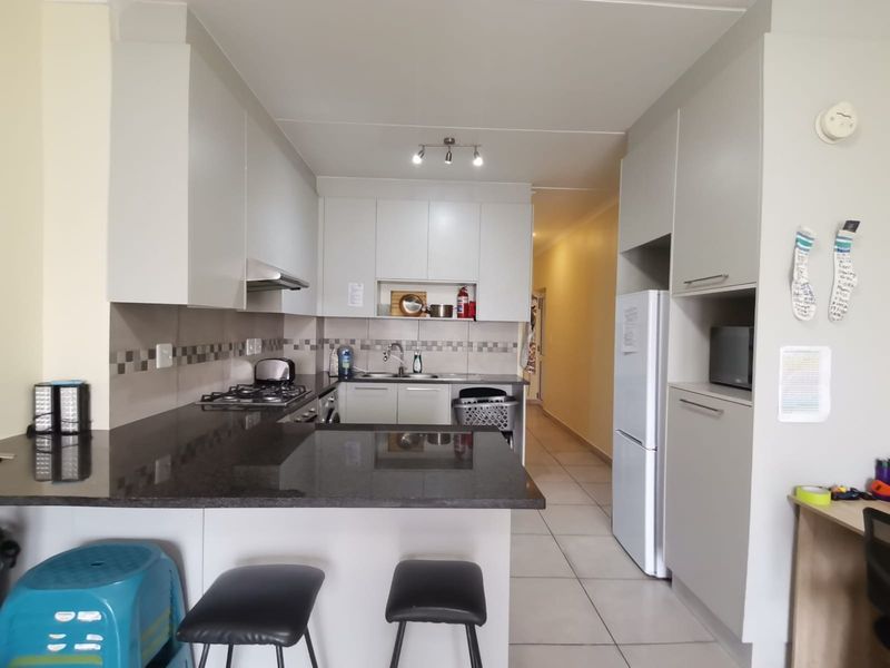 A functional kitchen featuring granite countertops, ample built-in cabinetry, a gas hob with extractor fan, and tiled flooring, leading into a hallway.