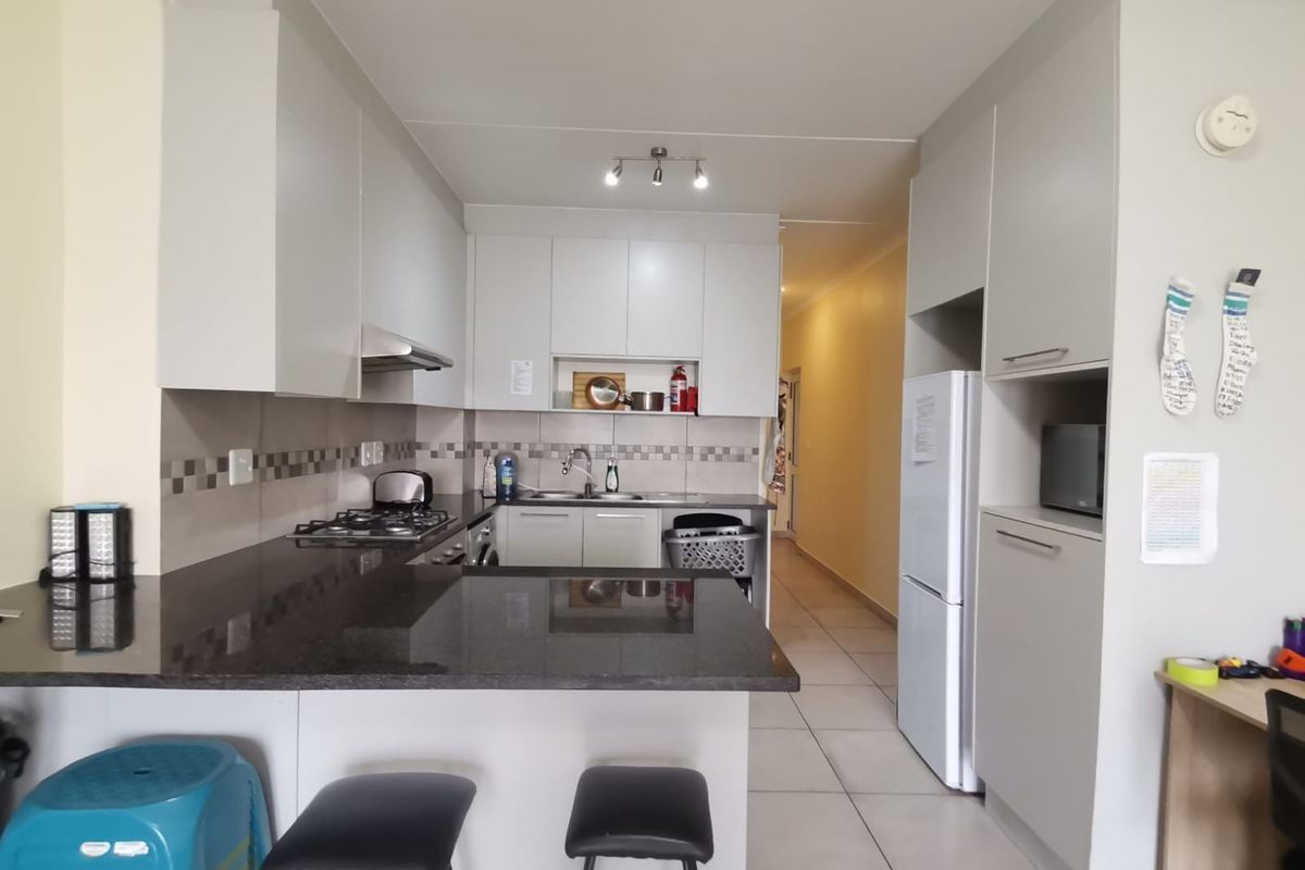A functional kitchen featuring granite countertops, ample built-in cabinetry, a gas hob with extractor fan, and tiled flooring, leading into a hallway.