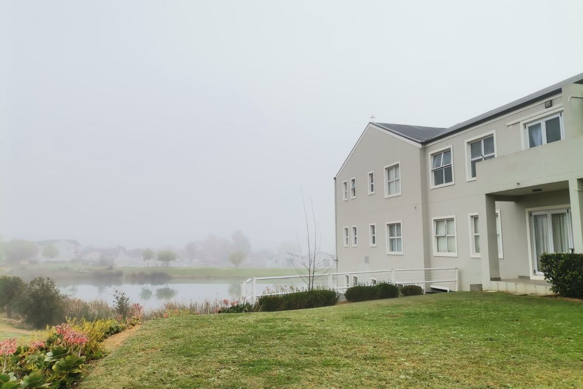 Rear view of the apartment building featuring a landscaped garden, balcony, and sliding door access, overlooking a tranquil pond area.