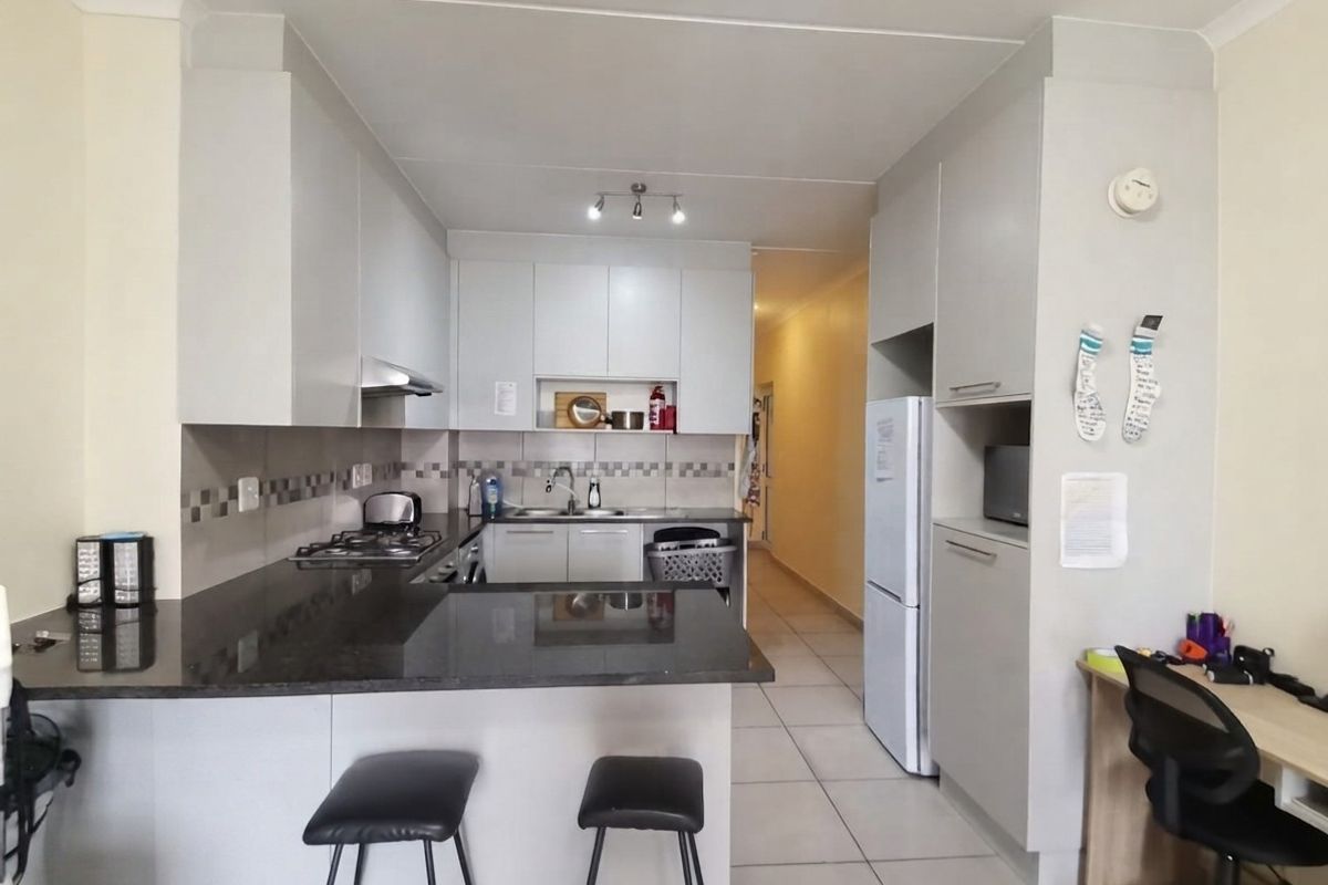 Modern kitchen featuring granite countertops, built-in cabinetry, gas hob, extractor fan, and tiled flooring, offering a functional and clean cooking space.