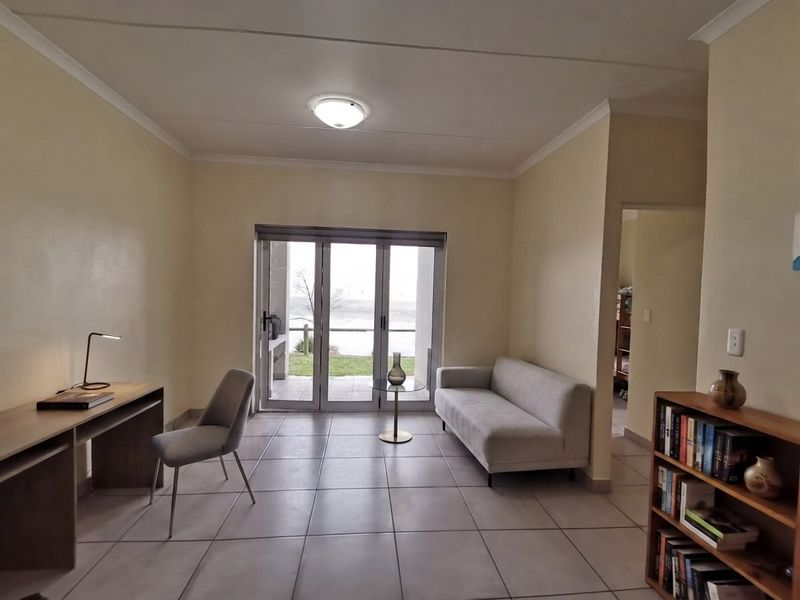 A bright living room featuring neutral tiled flooring and large sliding glass doors that provide access to an outdoor patio area.