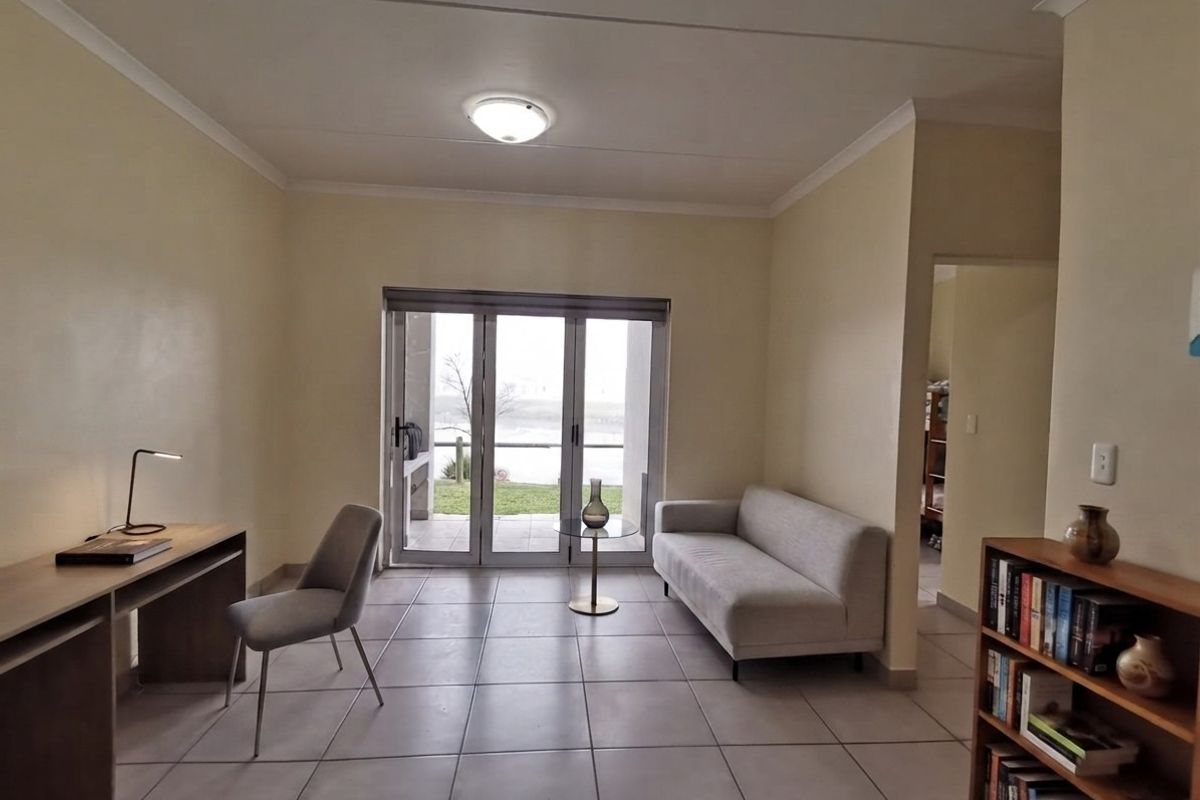 A bright living room featuring neutral tiled flooring and large sliding glass doors that provide access to an outdoor patio area.
