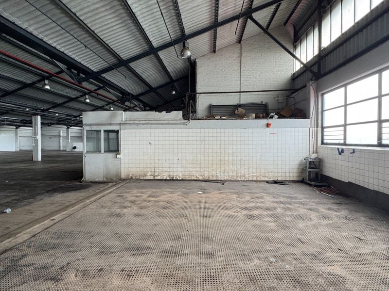 Spacious industrial utility area featuring high ceilings with exposed steel trusses, tiled wall partitions, and large windows providing ample natural light.