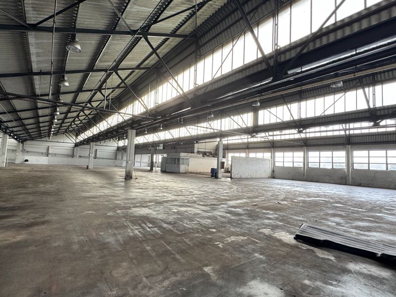Expansive industrial warehouse space featuring high ceilings with exposed steel trusses, clerestory windows for natural light, and durable concrete flooring.
