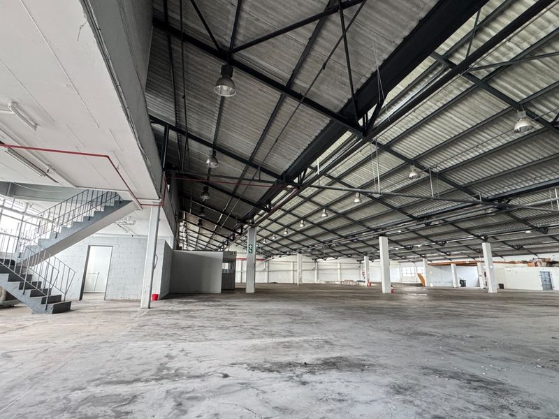 Spacious industrial warehouse featuring high ceilings with exposed steel trusses, concrete flooring, and an integrated metal staircase for mezzanine access.