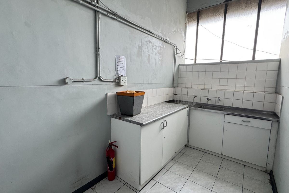 A functional industrial-style kitchenette featuring a stainless steel sink, tiled backsplash, and built-in cabinetry, requiring cosmetic updates to improve its overall condition.