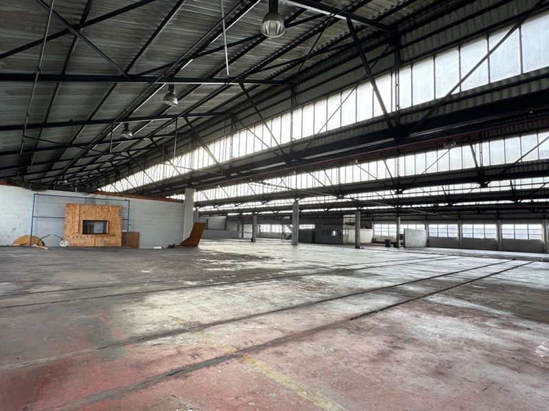 Expansive industrial warehouse space featuring high ceilings with exposed steel trusses, clerestory windows for natural light, and durable concrete flooring.