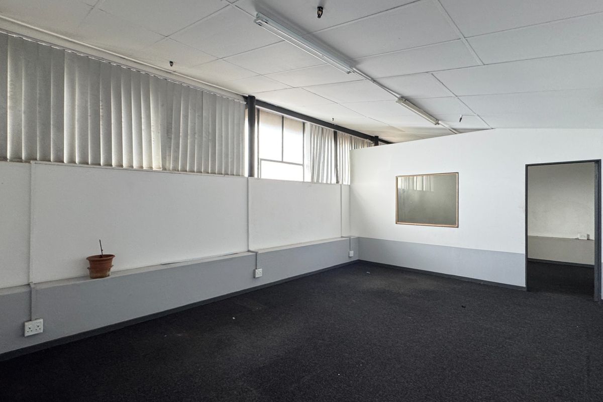 A vacant office space featuring a suspended ceiling, fluorescent lighting, vertical blinds, and a wall-mounted air conditioning unit.