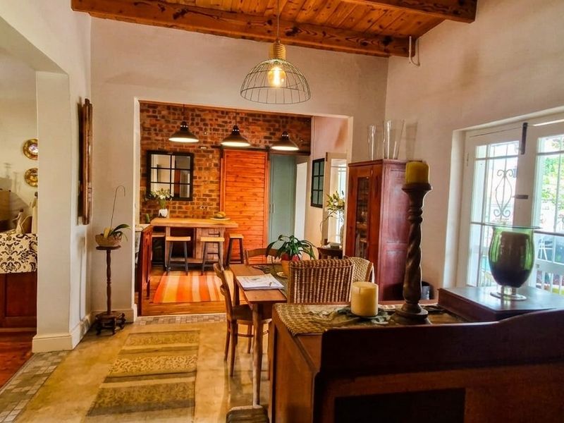An open-plan living and dining area featuring exposed timber ceiling beams, a rustic brick feature wall, and direct access to the outdoors via french doors.
