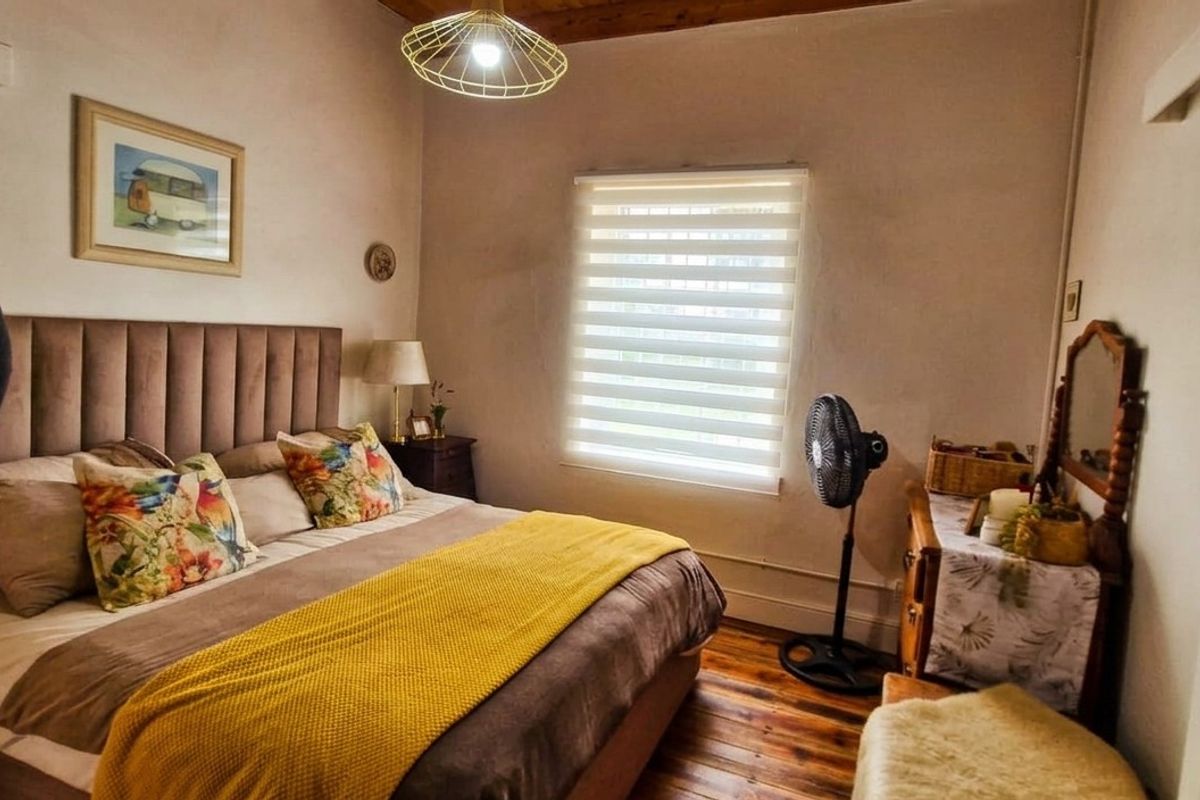 A cozy bedroom featuring warm timber flooring, exposed ceiling beams, and a modern roller blind, offering a comfortable and inviting living space.