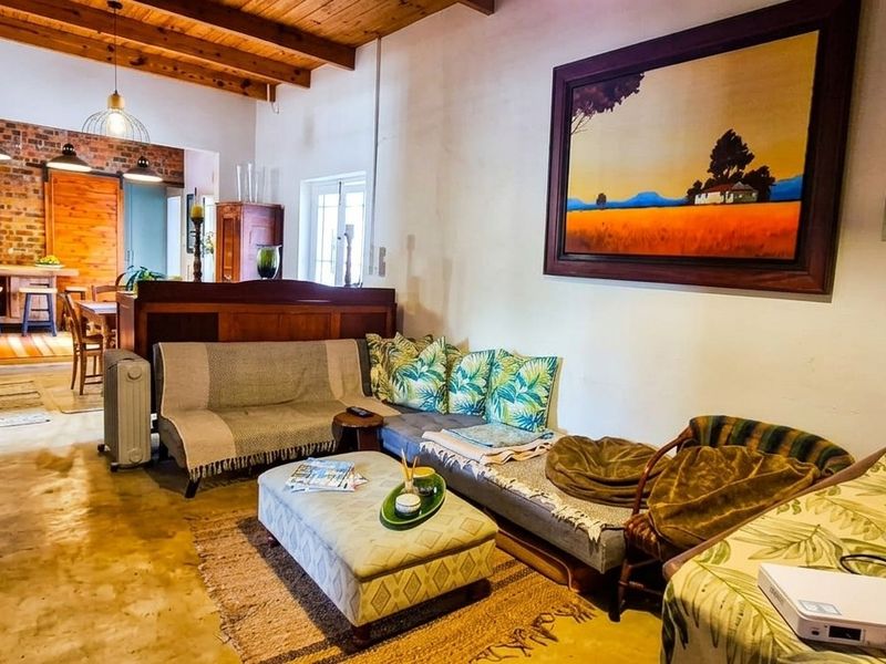 Open plan living area featuring exposed timber ceiling beams, polished concrete floors, and a rustic exposed brick accent wall leading into the kitchen space.