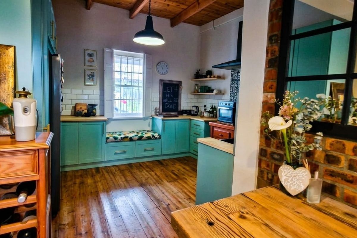 A charming kitchen featuring exposed timber beams, a brick feature wall, subway tile backsplash, and a cozy built-in window seat with timber flooring.