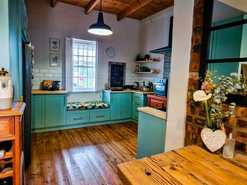 A charming kitchen featuring exposed timber beams, a brick feature wall, subway tile backsplash, and a cozy built-in window seat with timber flooring.