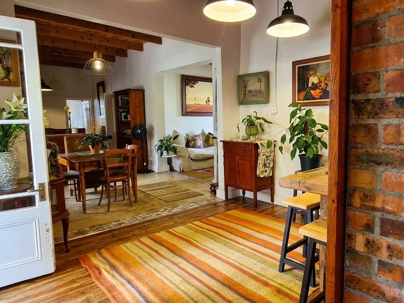 An inviting open-plan living and dining area featuring warm hardwood flooring, exposed timber ceiling beams, and a characterful exposed brick wall.