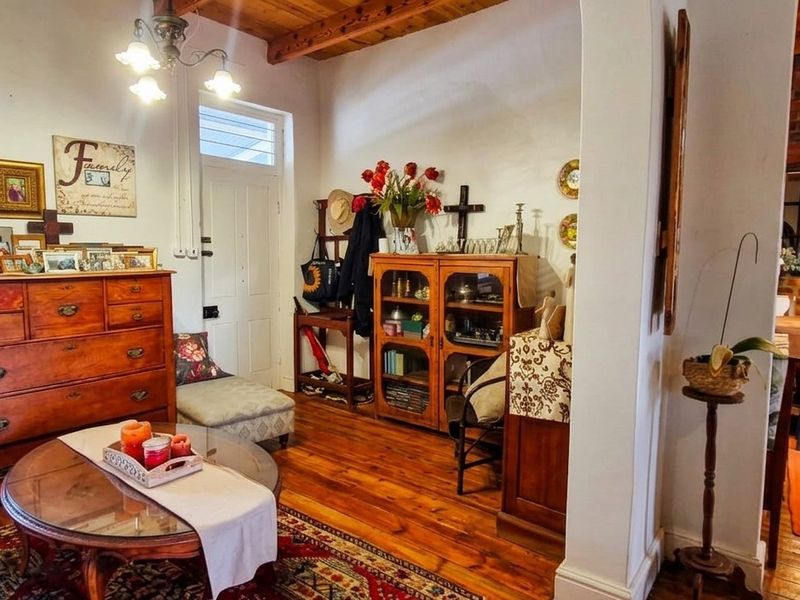 Open plan living area featuring exposed timber ceiling beams, warm hardwood flooring, and a rustic exposed brick wall connecting to the kitchen space.