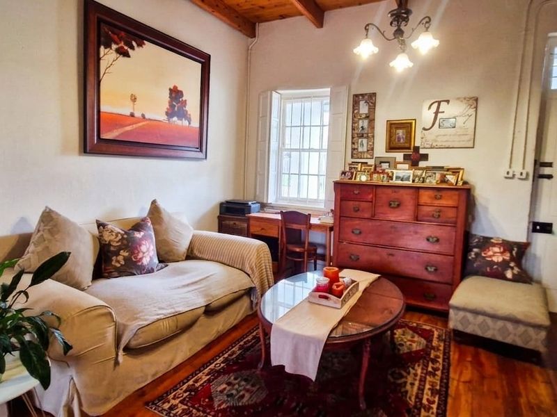 A cozy living room featuring exposed timber ceiling beams, warm timber flooring, and a classic sash window, creating a comfortable and inviting atmosphere.