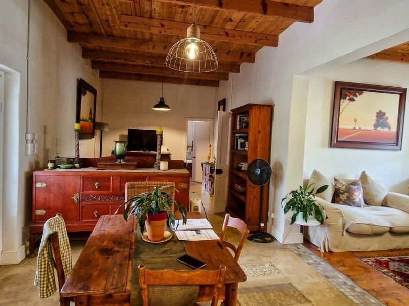 Open plan living and dining area featuring exposed timber beam ceilings, concrete flooring, and direct access to an outdoor space via a glass panel door.