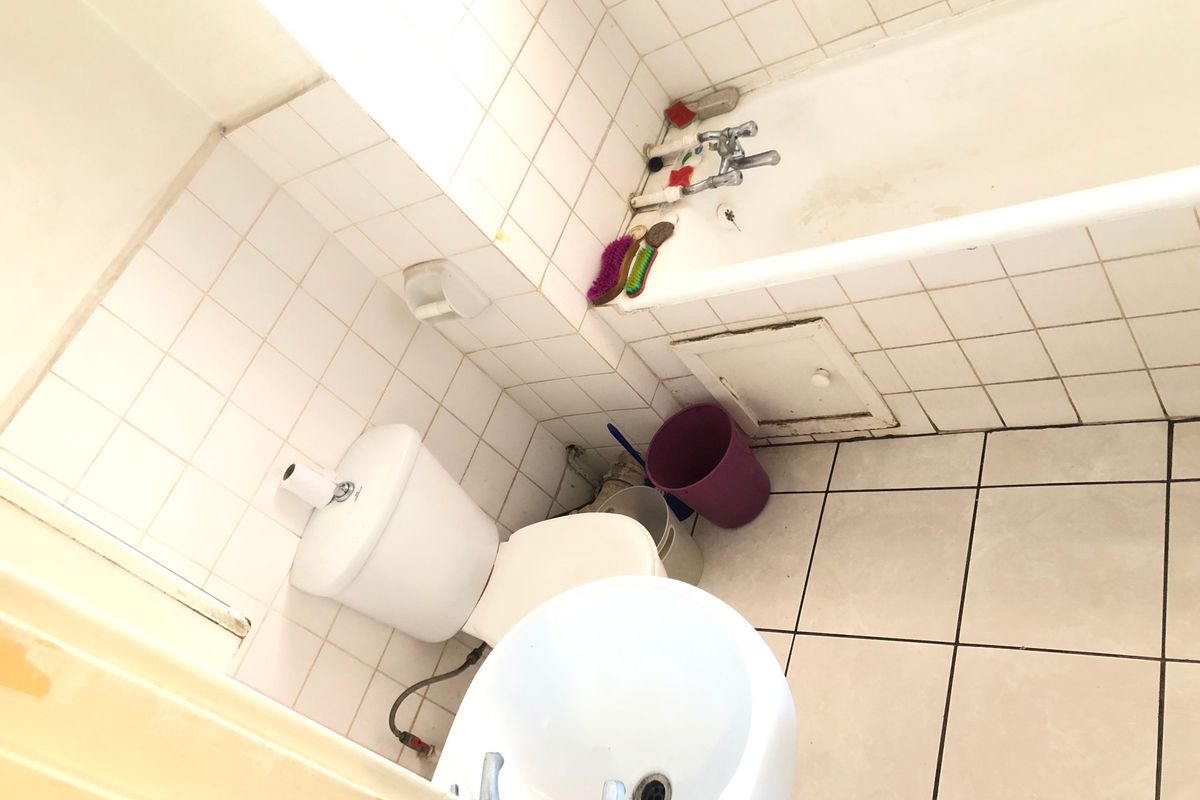A dated bathroom featuring a standard bathtub, toilet, and pedestal basin with white ceramic wall and floor tiling.