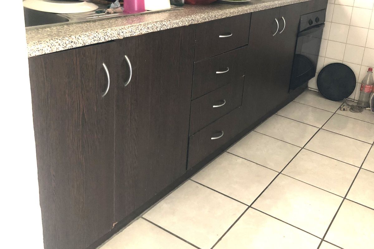 A functional kitchen featuring dark wood-grain cabinetry, a granite-look laminate countertop, built-in oven, and tiled flooring.