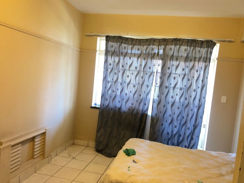 A bedroom featuring tiled flooring, a built-in wall vent, and a picture rail, requiring cosmetic updates to improve its overall condition.