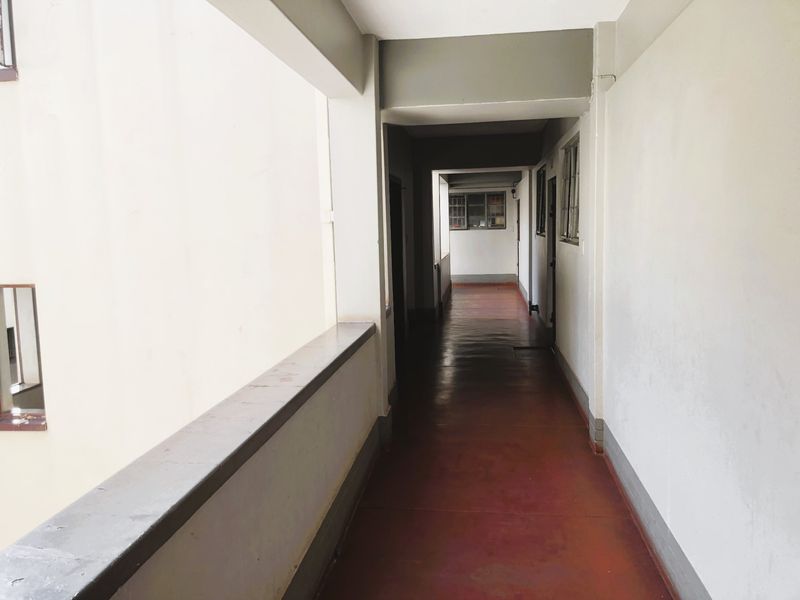 A long, open-air apartment building corridor featuring painted concrete flooring and a concrete balustrade, providing access to multiple residential units.