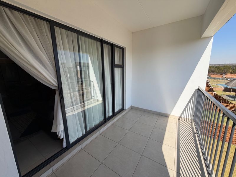A clean, modern balcony featuring tiled flooring, a metal balustrade, and large sliding glass doors providing access to the interior living space.