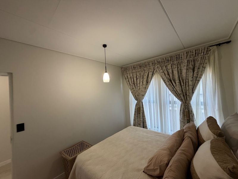 A well-maintained bedroom featuring neutral walls, a modern pendant light fixture, and floor-to-ceiling window treatments.