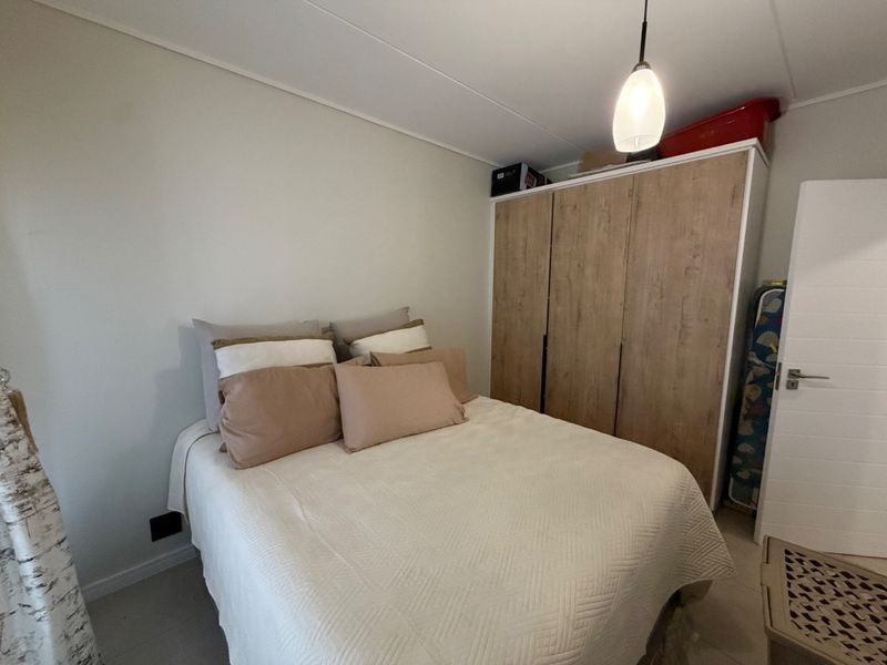 A functional bedroom featuring a built-in wooden wardrobe and a modern pendant light fixture.
