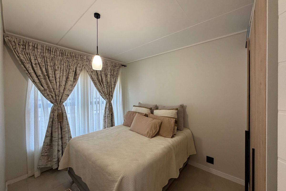 A well-maintained bedroom featuring neutral tiled flooring, a built-in wardrobe, and a modern pendant light fixture.