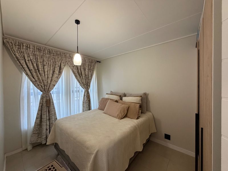 A well-maintained bedroom featuring neutral tiled flooring, a built-in wardrobe, and a modern pendant light fixture.