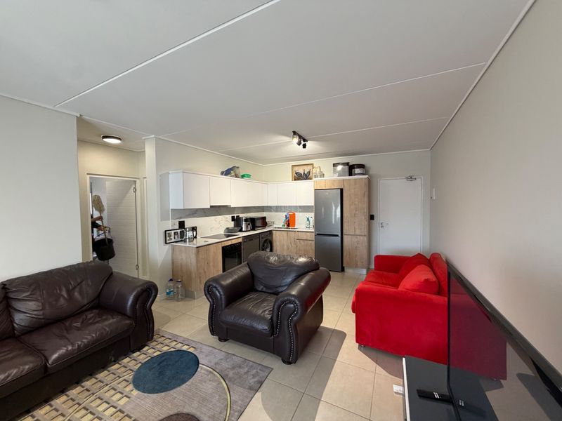 Open-plan living area featuring a modern kitchen with built-in cabinetry, integrated appliances, and tiled flooring throughout the combined space.