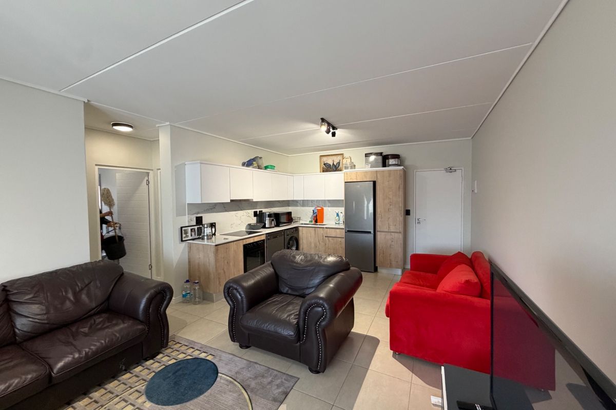 Open-plan living area featuring a modern kitchen with built-in cabinetry, integrated appliances, and tiled flooring throughout the combined space.