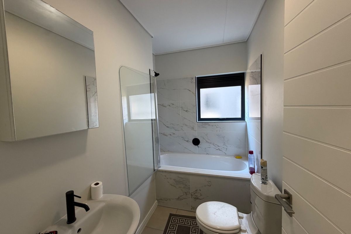 Modern bathroom featuring marble-look wall tiles, a bathtub with a glass screen, black tapware, and a pedestal basin.