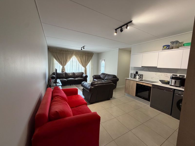 Open-plan living area featuring a modern kitchen with built-in cabinetry, electric hob, oven, and tiled flooring throughout the combined space.