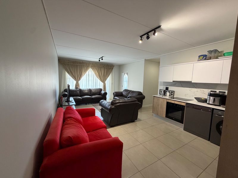 Open-plan living area featuring a modern kitchen with built-in cabinetry, electric hob, oven, and tiled flooring, seamlessly flowing into the lounge space.