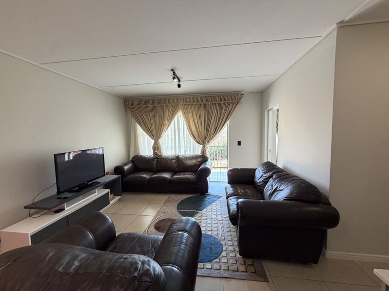 A spacious living room featuring neutral tiled flooring, track lighting, and a sliding glass door providing access to an outdoor area.
