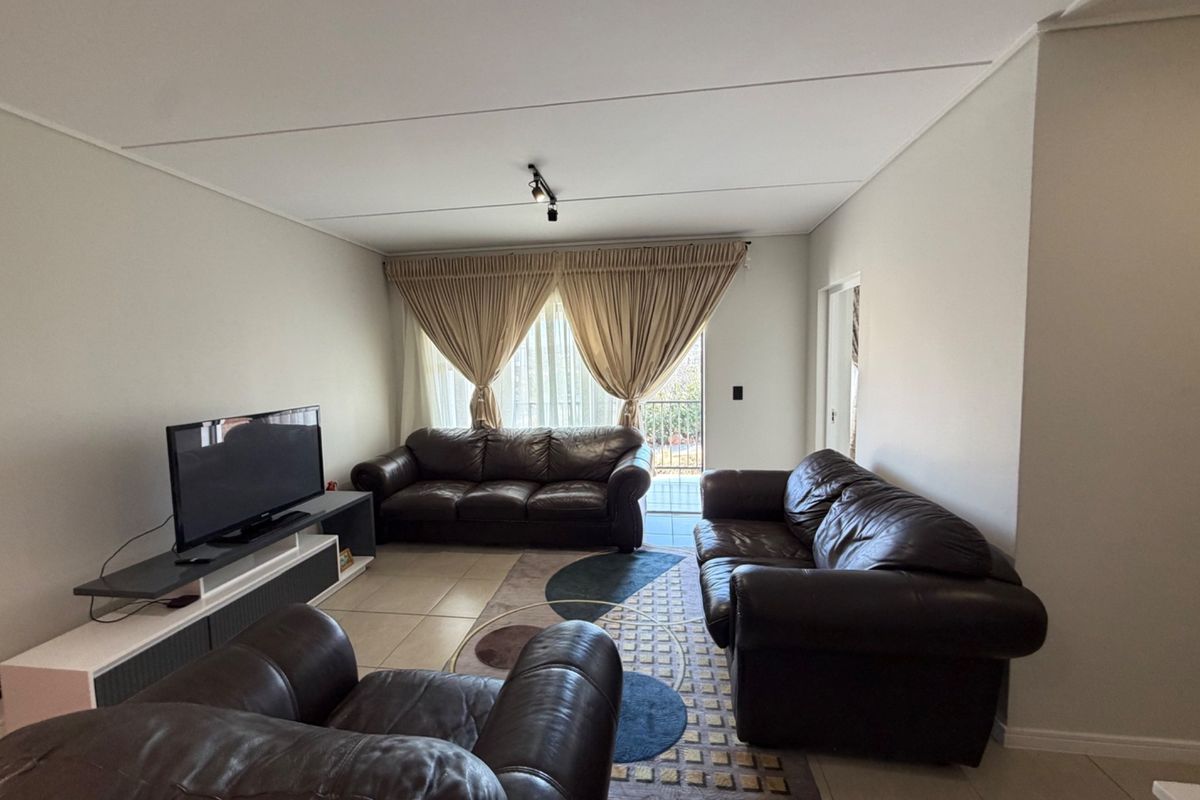 A spacious living room featuring neutral tiled flooring, track lighting, and a sliding glass door providing access to an outdoor area.