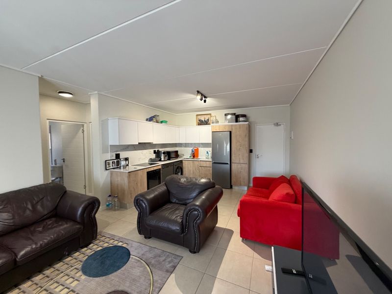 Open-plan living area featuring a modern kitchen with built-in cabinetry, stone-look countertops, and tiled flooring, seamlessly connected to the lounge space.
