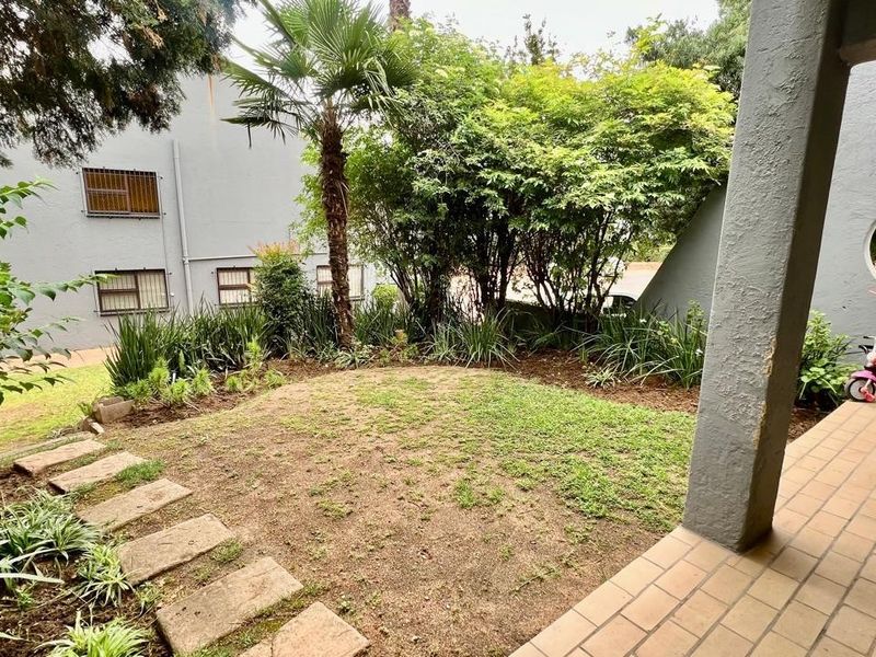 A covered patio area featuring tiled flooring and a unique circular architectural opening, overlooking a private garden space with stone pathways.