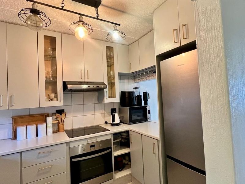 Compact kitchen featuring white cabinetry, tiled backsplash, built-in oven, electric hob, and modern track lighting.