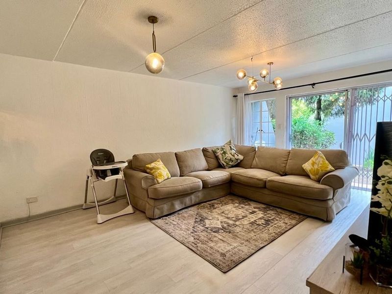 A bright living room featuring light-toned laminate flooring, modern pendant lighting, and a large sliding glass door providing access to the exterior.
