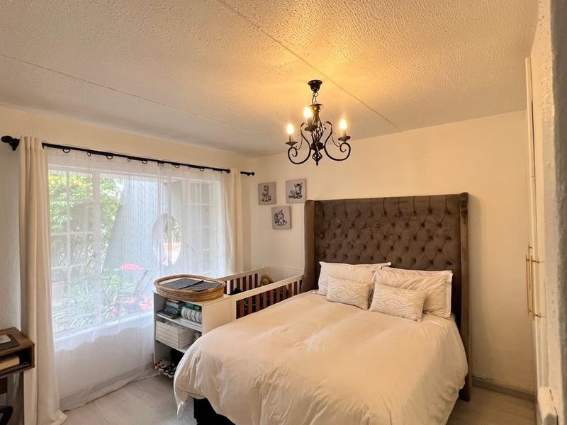 A cozy bedroom featuring a built-in wardrobe, a decorative chandelier, and a large window allowing natural light into the space.