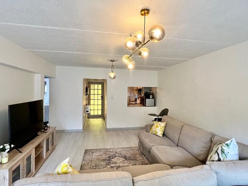 Spacious living room featuring light laminate flooring, textured ceilings, modern pendant lighting, and a convenient pass-through window connecting to the kitchen area.