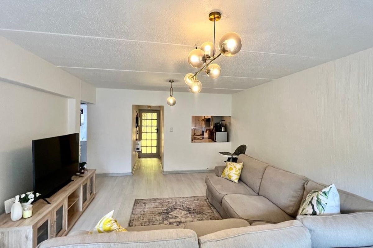 Spacious living room featuring light laminate flooring, textured ceilings, modern pendant lighting, and a convenient pass-through window connecting to the kitchen area.