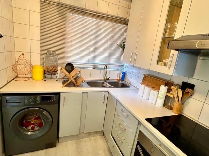Compact kitchen featuring built-in cabinetry, laminate countertops, integrated oven, electric hob, extractor fan, and a stainless steel sink with tiled splashback.