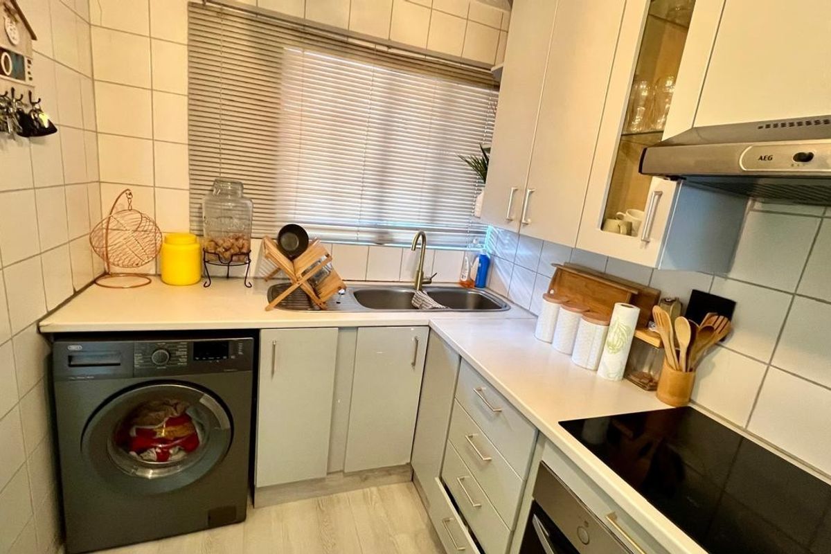 Compact kitchen featuring built-in cabinetry, laminate countertops, integrated oven, electric hob, extractor fan, and a stainless steel sink with tiled splashback.